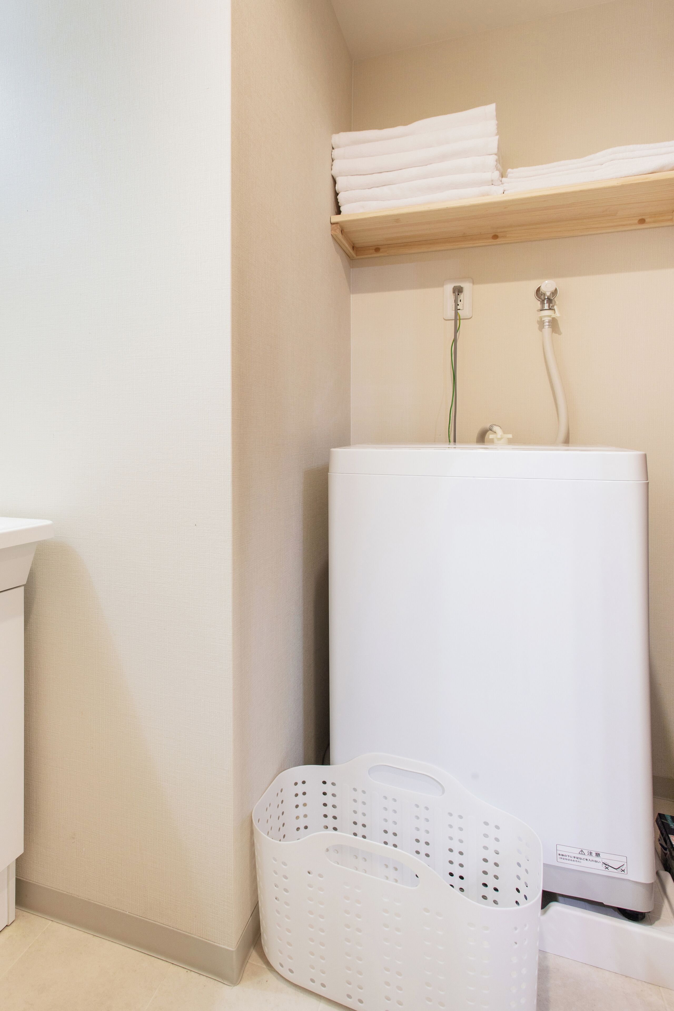 A laundry room with a washing machine, a white basket, and a shelf with folded towels.