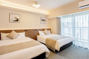 Quarto de hotel com duas camas, cabeceira de madeira, uma janela grande com cortinas finas e ar condicionado fixado na parede.