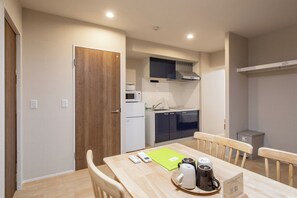 A compact kitchen with a microwave, stove, and cabinets, a dining table with chairs, and a small trash bin. - Star house (Osaka)