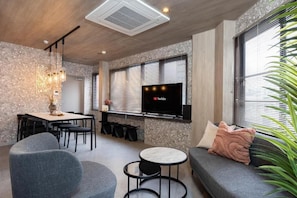 A modern living room with a dining area, a flat-screen TV mounted on the wall, and a large window with blinds. - JAPAVISTA Vita (BENTEN, MINATO WARD)