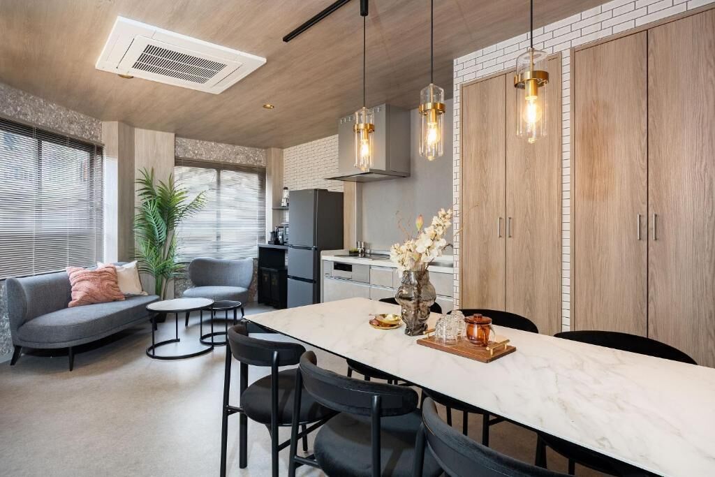 A modern kitchen with a marble countertop, pendant lights, and wooden cabinets.