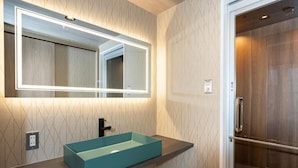 Een badkamer met een rechthoekig wastafel, een spiegel met verlichting en een douchedeur.