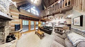 L’intérieur d’un chalet rustique, avec un mur en pierre, des poutres en bois, une cheminée, un canapé, une table basse et un coin cuisine.
