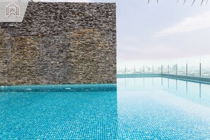 A swimming pool with a stone wall and a city skyline view. - Уютный номер на высоком этаже с потрясающим видом на реку Чаопрайя (Chang Wat Nonthaburi)