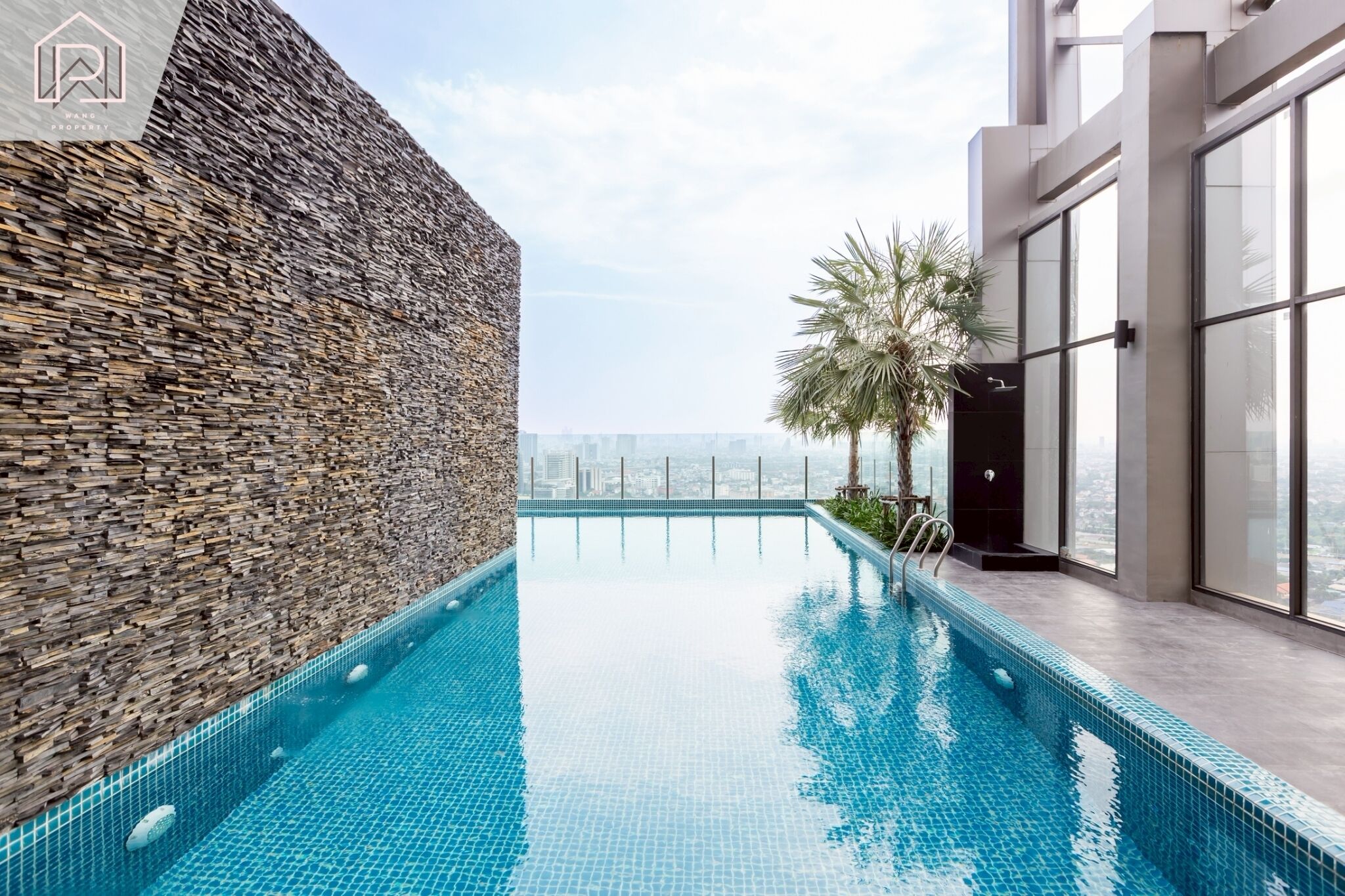 Ein Pool mit Infinity-Kante auf dem Dach, mit einer Steinmauer und einem modernen Glasgebäude.