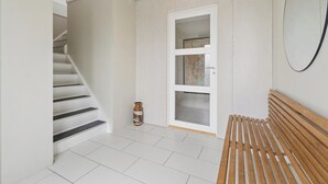 Una escalera conduce a una habitación con un banco de madera, una puerta blanca y un pequeño jarrón.