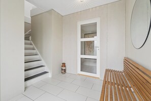 Un escalier menant à une pièce où se trouvent un banc en bois, une porte blanche et un petit vase.