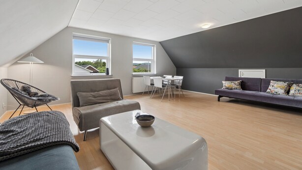 Un loft moderno con techo inclinado, comedor, sofá y una silla.