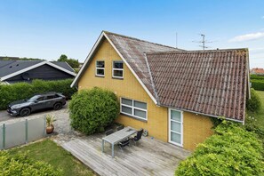 A residential house with a tiled roof, a car parked in the driveway, a patio with a table and chairs, and a well-maintained garden. - Holiday apartment in Nexø close to beach and port (Nexø)