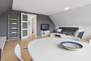 A modern room with a white dining table, a sofa, a TV, and a bookshelf. - Holiday apartment in Nexø close to beach and port (Nexø)