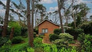 A small brick house surrounded by dense greenery and tall trees. - Holiday Home in Beekbergen With Terrace (Beekbergen)