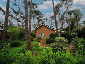A small brick house surrounded by dense greenery and tall trees. - Holiday Home in Beekbergen With Terrace (Beekbergen)