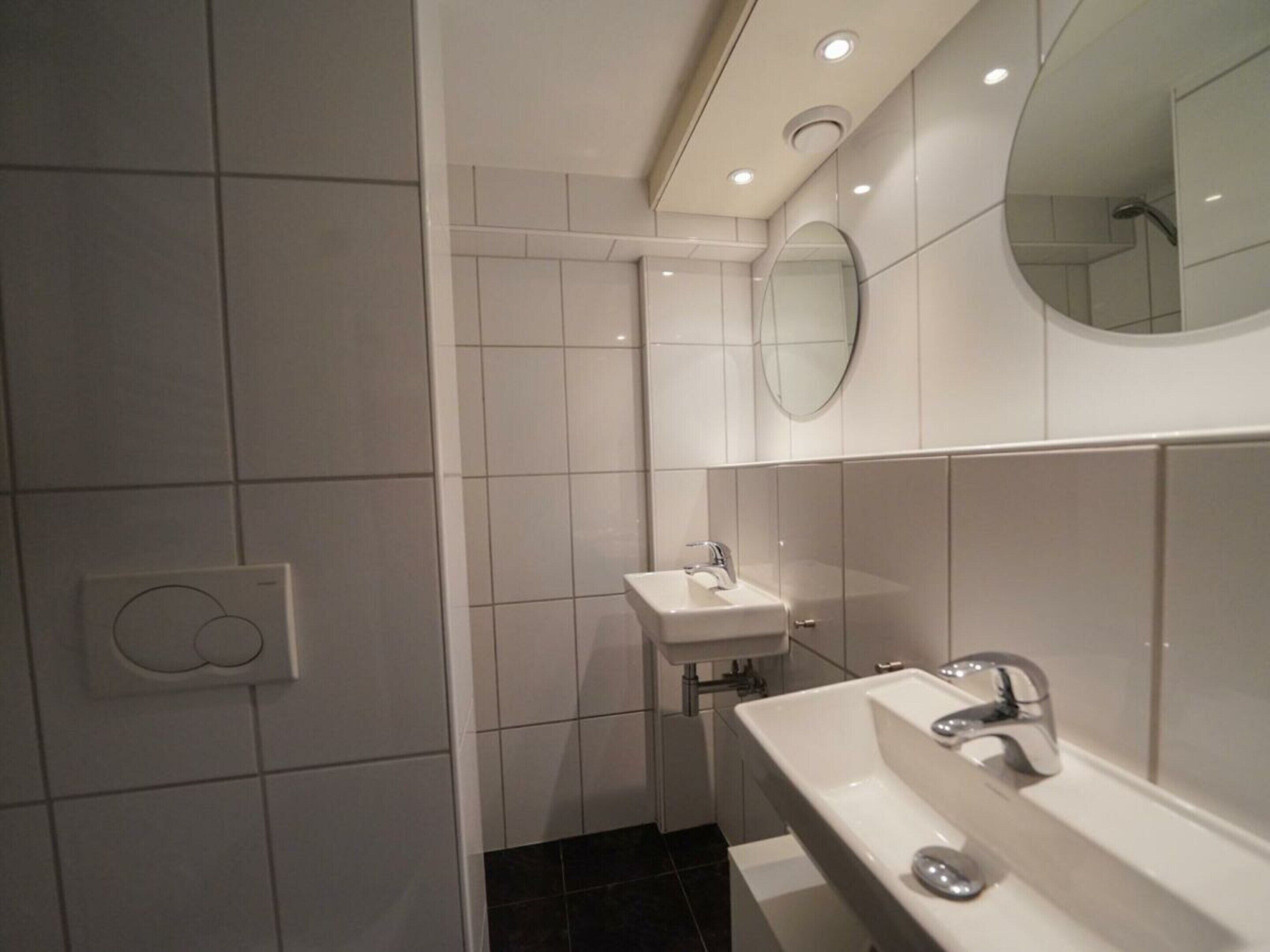 A modern bathroom with a white sink, mirror, and tiled walls.