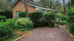 A brick house with a sloped roof, surrounded by dense greenery and trees. - Holiday Home in Beekbergen With Terrace (Beekbergen)