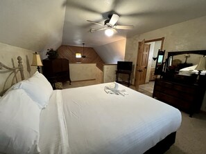 Une chambre à coucher comprenant un lit, un ventilateur de plafond, une commode et un bureau.