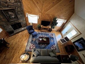 Une pièce aux hauts plafonds, dot ée d’une cheminée en pierre, d’un canapé bleu, d’un tapis à motifs et d’une table basse en bois.