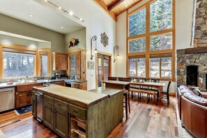 A spacious kitchen with a large island, wooden cabinets, and a stone fireplace. - Luxury Cabin with a Private Hot Tub in Tahoe Donner, California (Truckee)