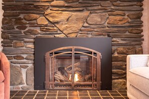 A stone fireplace with a metal front, a fire burning inside, and a tiled floor.