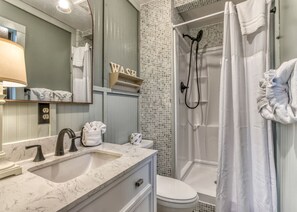 A bathroom with a sink, mirror, towel rack, shower, and toilet.