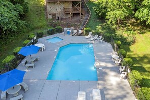 A rectangular pool with a wooden deck, surrounded by white lounge chairs and umbrellas, with a stone building in the background.