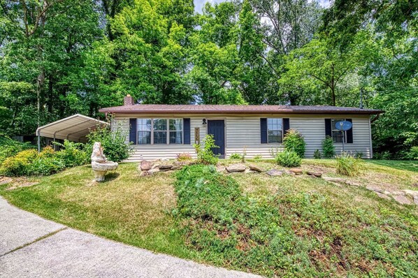 A single-story house with a front porch, a satellite dish, and a stone sculpture in the yard.