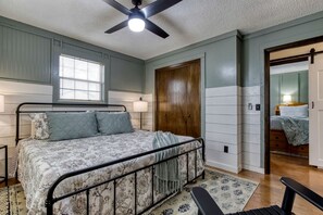 A bedroom with a bed, a ceiling fan, a window, a door, and a nightstand.