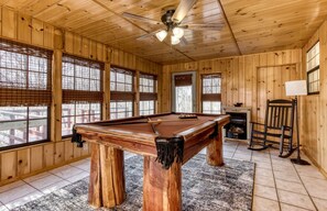 A wooden room with a pool table, a ceiling fan, and a fireplace.