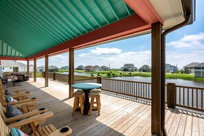 Une terrasse en bois avec des sièges d’extérieur, une table et une vue sur un plan d’eau et des maisons.