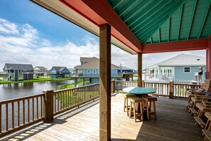 Une terrasse en bois avec une table et des chaises, donnant sur une étendue d’eau et sur des maisons.