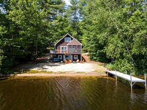 A house with a dock extending into a lake, surrounded by dense trees. - Idyllic Waterfront Lakehouse in Barnstead, New Hampshire (Barnstead)