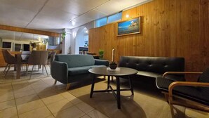 A modern interior with a dining area, sofas, and a wooden accent wall. - Cozy Lodge In Tarcoola Beach | Coastal Retreat (Tarcoola Beach)