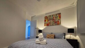 A bedroom with a large bed, a painting on the wall, and a nightstand with a lamp. - Cozy Lodge In Tarcoola Beach | Coastal Retreat (Tarcoola Beach)
