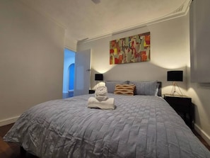 Ein Schlafzimmer mit einem großen Bett, einem Bild an der Wand und einem Nachttisch mit einer Lampe.