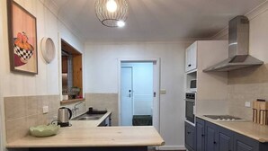 A kitchen with a central island, grey cabinets, a stainless steel range hood, and a hanging light fixture. - Cozy Lodge In Tarcoola Beach | Coastal Retreat (Tarcoola Beach)