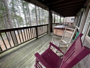 Eine überdachte Veranda mit Holzgeländern, einem roten Adirondack-Sessel und einem Tisch mit Stühlen.