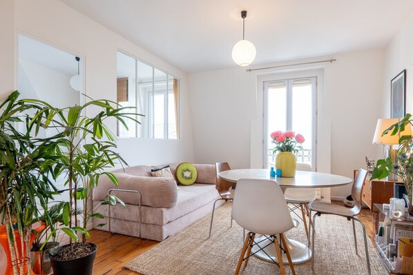 A modern living room with a sofa, dining table, chairs, and potted plants. - Charming Montmartre Stay Near Metro & Local Cafés (Paris)