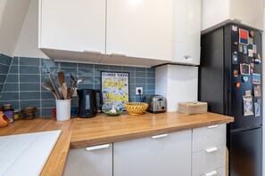 A kitchen with a wooden countertop, white cabinets, a black refrigerator, and a poster on the wall. - Charming Montmartre Stay Near Metro & Local Cafés (Paris)