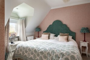 Une chambre avec un plafond en pente, un lit doté d’une tête de lit verte, deux tables de chevet avec des lampes et une fenêtre avec des rideaux.