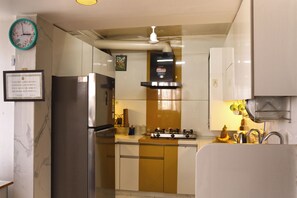 A kitchen with a refrigerator, stove, sink, and a clock on the wall. - 3BR Borderman's Retreat in center with cook (Jaipur)