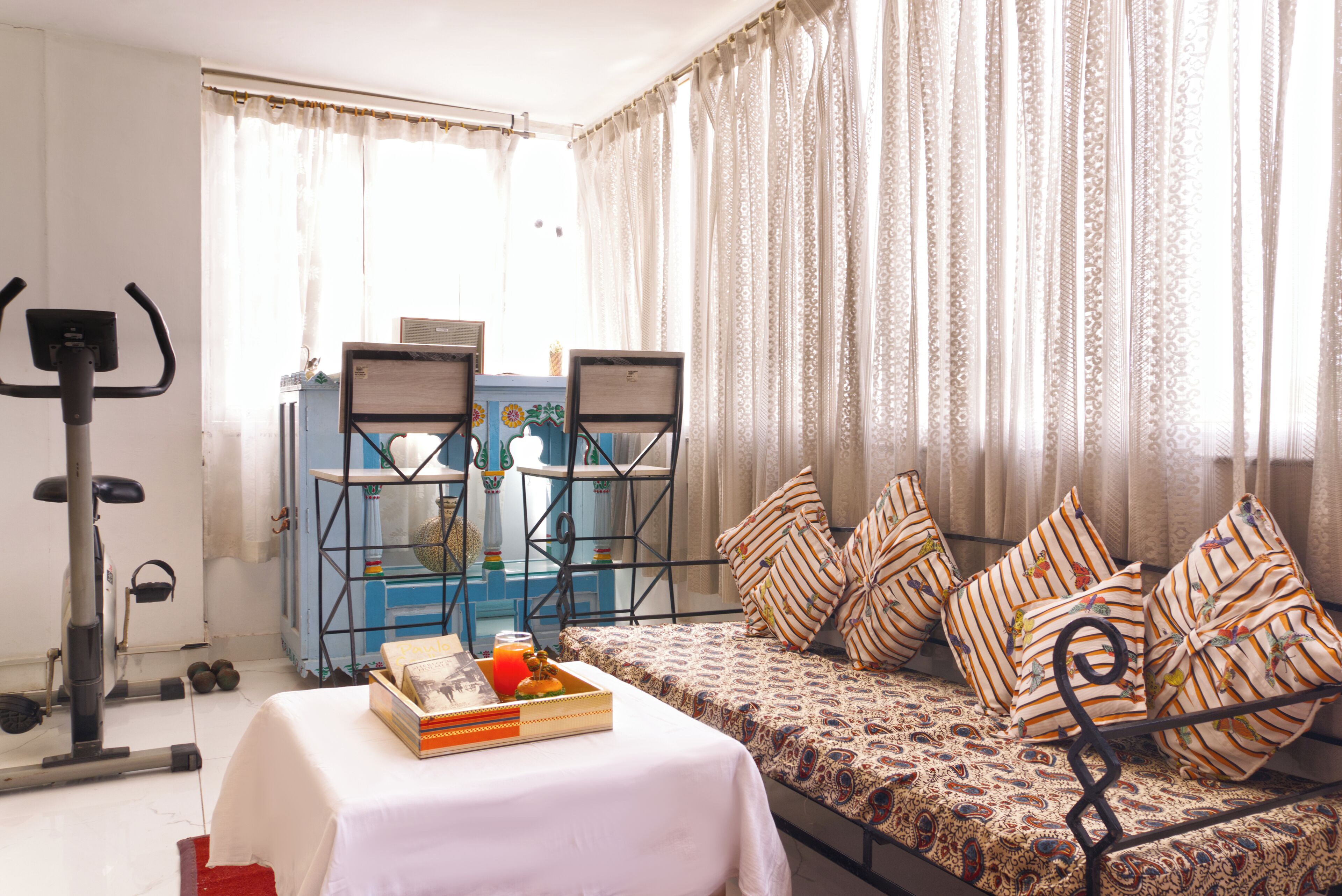 A room with a bed, a table with a tray of food, a treadmill, and a window with curtains.