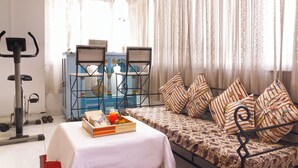 Una habitación con una cama, una mesa con una bandeja de comida, una caminadora y un ventanal con cortinas.