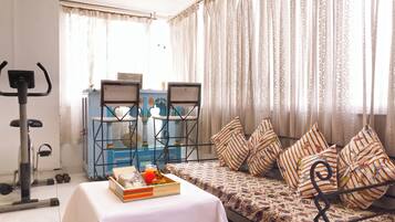 A room with a bed, a table with a tray of food, a treadmill, and a window with curtains.