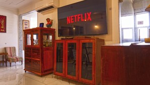 Una sala de estar con una televisión mostrando 'NETFLIX', un mueble de madera y un sillón estampado.
