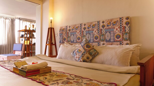 Una cama bien hecha con colcha estampada, una mesita de noche con lámpara y una pared con azulejos decorativos.