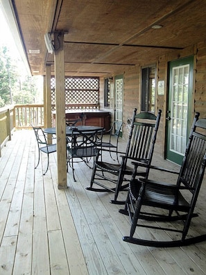 Een houten terras met schommelstoelen en een tafel, een overdekt gedeelte met een balustrade, en uitzicht op de omgeving.