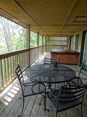 Een overdekt terras met een ronde metalen tafel en stoelen, een houten bank en een hottub.