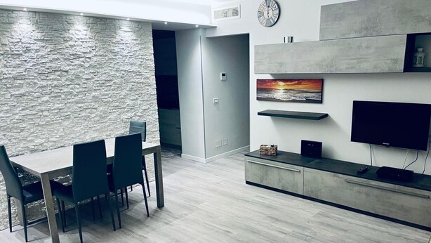A modern kitchen with a stone wall, a dining table with chairs, a flat-screen TV, and a built-in shelf. - S375 - Sirolo, three-room apartment with private courtyard (SIROLO)
