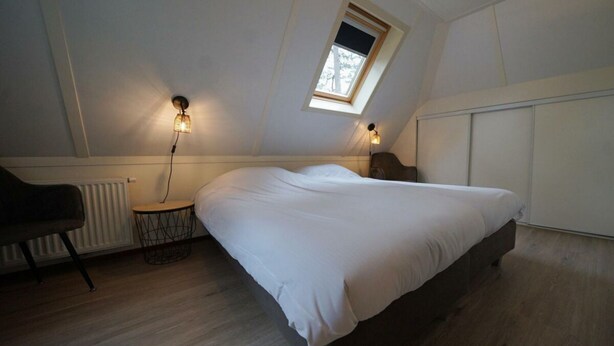 Ein Schlafzimmer mit Bett, Sessel, kleinem Tisch, Heizkörper und Dachfenster.