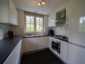 A modern kitchen with white cabinets, a black countertop, a window, a stove, and a microwave.