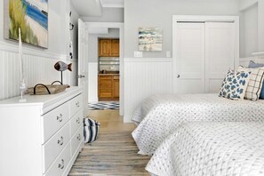 Ein Schlafzimmer mit Bett, Kommode und Blick zur Küche.